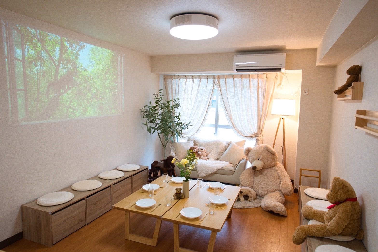 Moff room名古屋店の室内全体。木のローテーブル2台に取り皿が並び、壁際にはベンチ収納、正面の壁にはプロジェクターで緑の映像が映し出されている