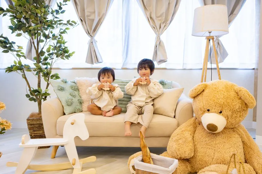 Moff room三宮店のソファで、2人の子どもが並んで座りパンを食べている。そばに白い木馬と大きなくまのぬいぐるみがある