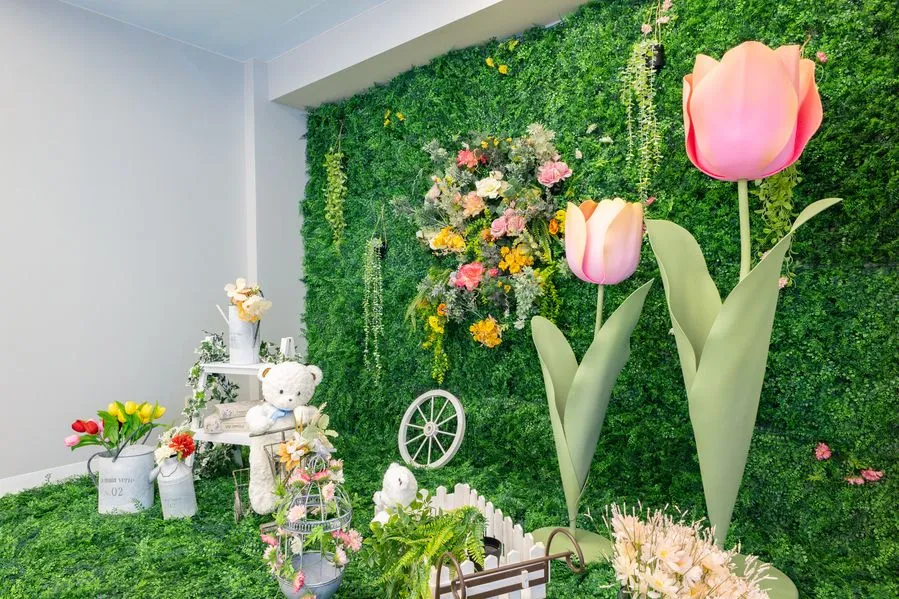 Moff room三ノ宮店の花壁の撮影ブース。緑の壁に花のリースと大きなチューリップのオブジェを飾り、白いくまのぬいぐるみとブリキのバケツに入れたチューリップを置いている