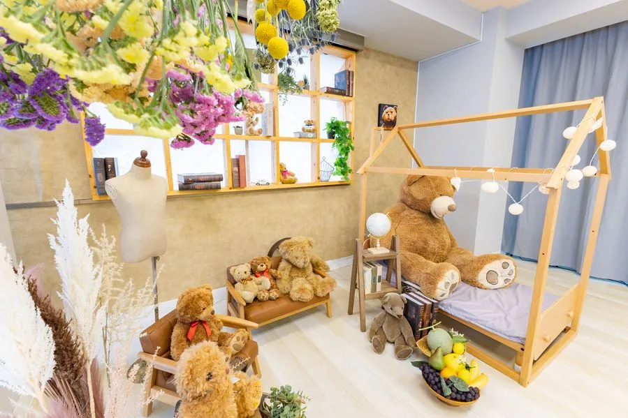 Moff room三ノ宮店の撮影スペース。天井から吊るしたドライフラワーと木製の飾り棚、大きなくまのぬいぐるみを乗せた木のベッド