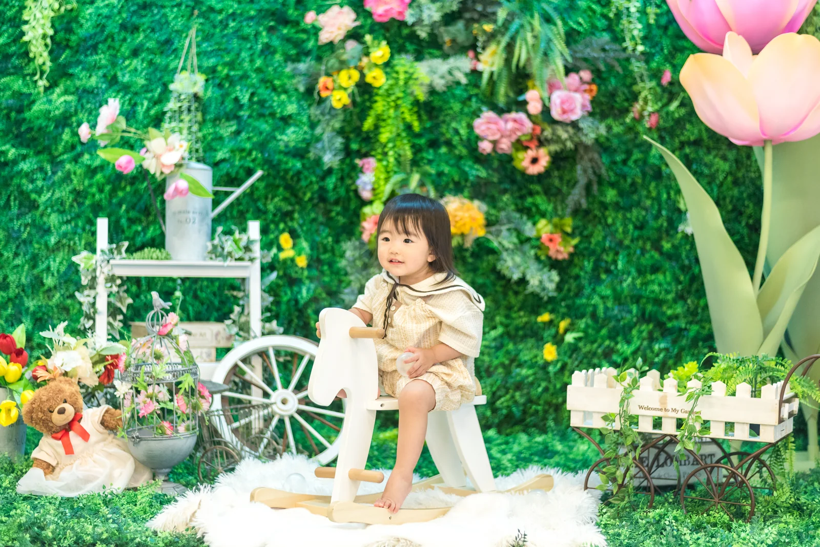 三ノ宮店の花と緑の背景の前で、白い木馬に座る子どもの撮影例